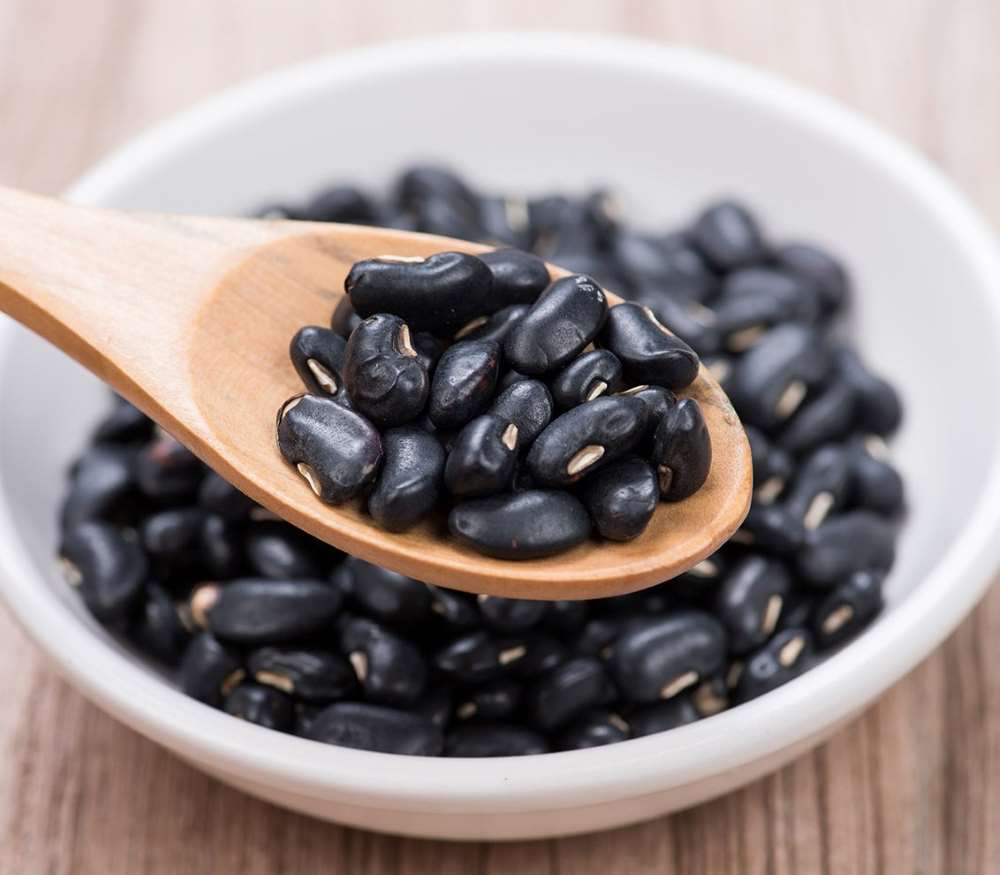 Black beans in a wooden spoon, in a bowl.