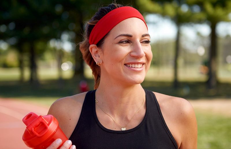 Woman smiling, walking outside, with a shaker bottle.