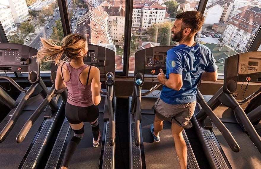 A man and woman running side by side on treadmills, in a highrise.