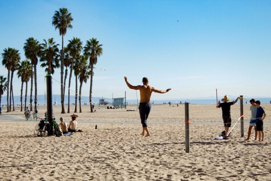 Man on tightrope, between two palm trees, at the beach.