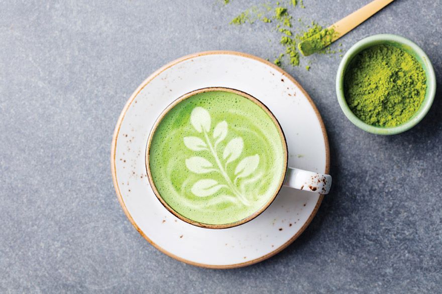 A moringa latte, with a tree design on top, in a white cup.